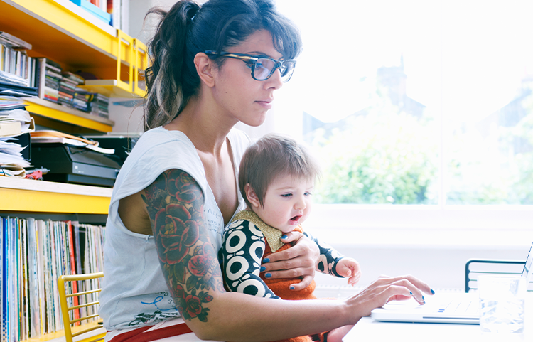 Une mère avec des lunettes s’assoit avec son bébé sur ses genoux pendant qu’elle regarde un ordinateur portable.